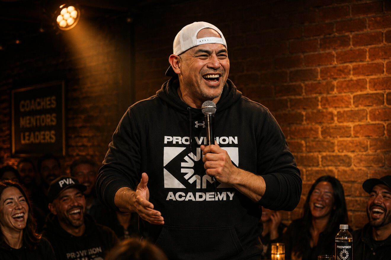 A coach in a Pro Vision Academy hoodie performing stand-up to a laughing crowd
